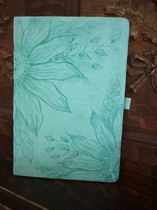 Green notebook with floral embossing on a wooden surface