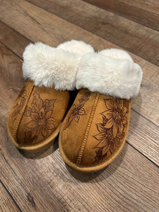 Pair of brown slippers with white fur lining on a wooden floor.
