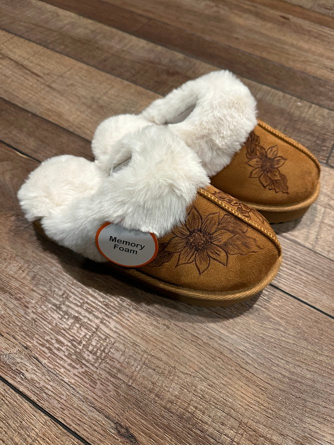 Pair of brown slippers with white fuzzy interior on a wooden floor.