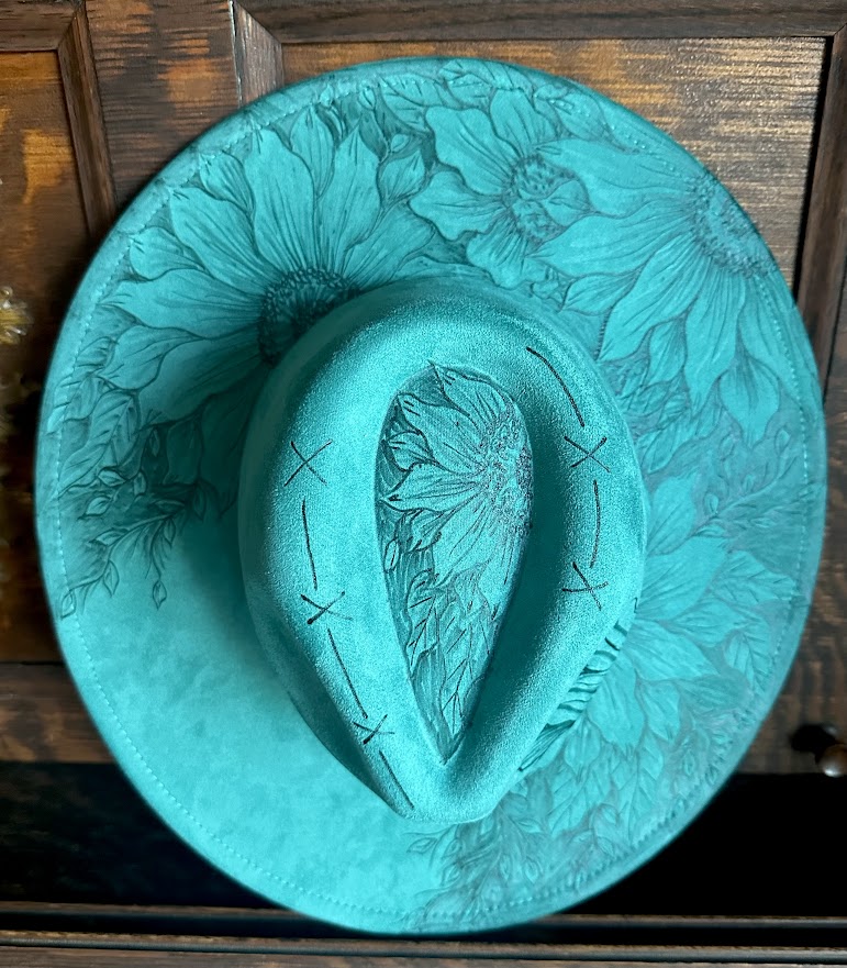 Turquoise cowboy hat with floral embossing on a wooden surface