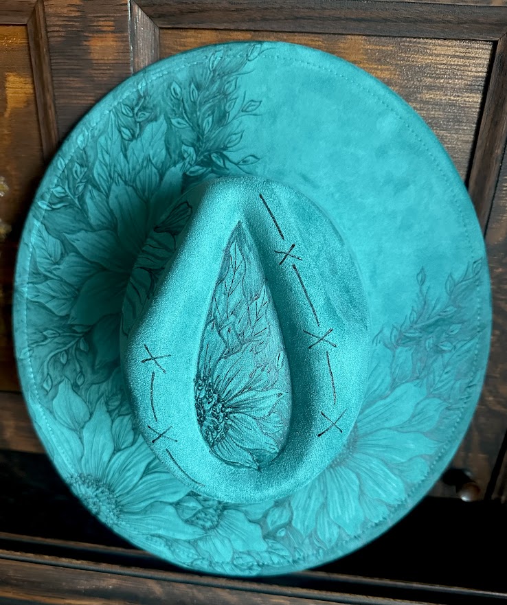 Turquoise cowboy hat with floral patterns on a wooden surface