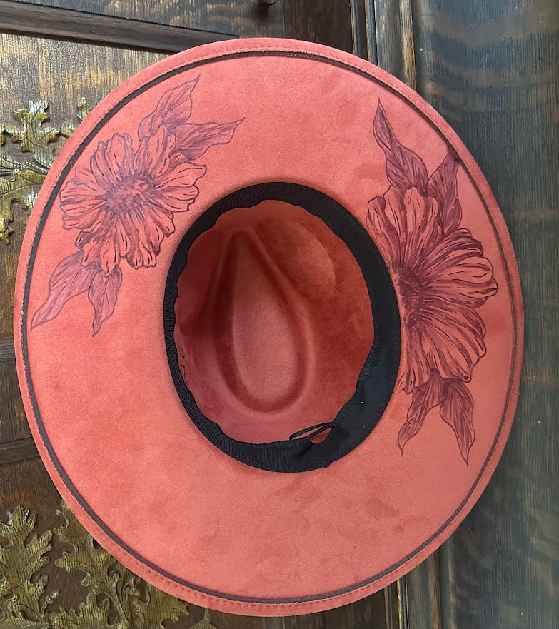 Pink cowboy hat with floral designs on a wooden surface
