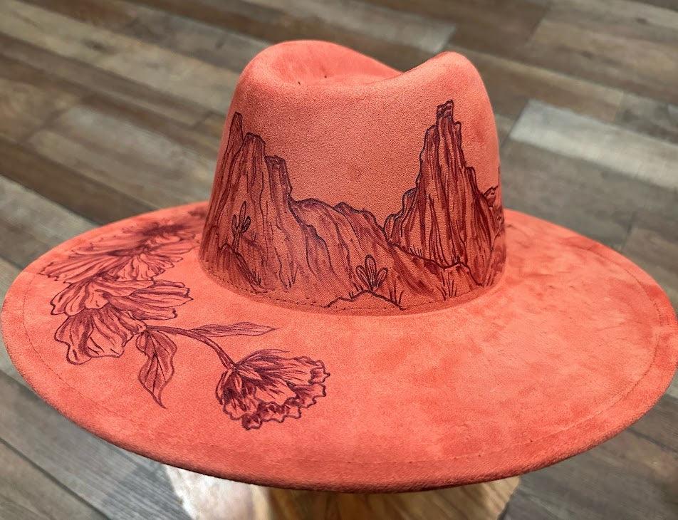 Pink cowboy hat with mountain and flower designs on a wooden surface