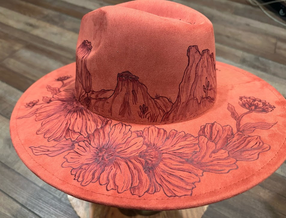 Pink hat with engraved desert landscape and flowers on a wooden surface