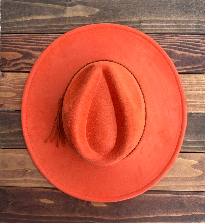 Orange cowboy hat with a tassel on a wooden surface