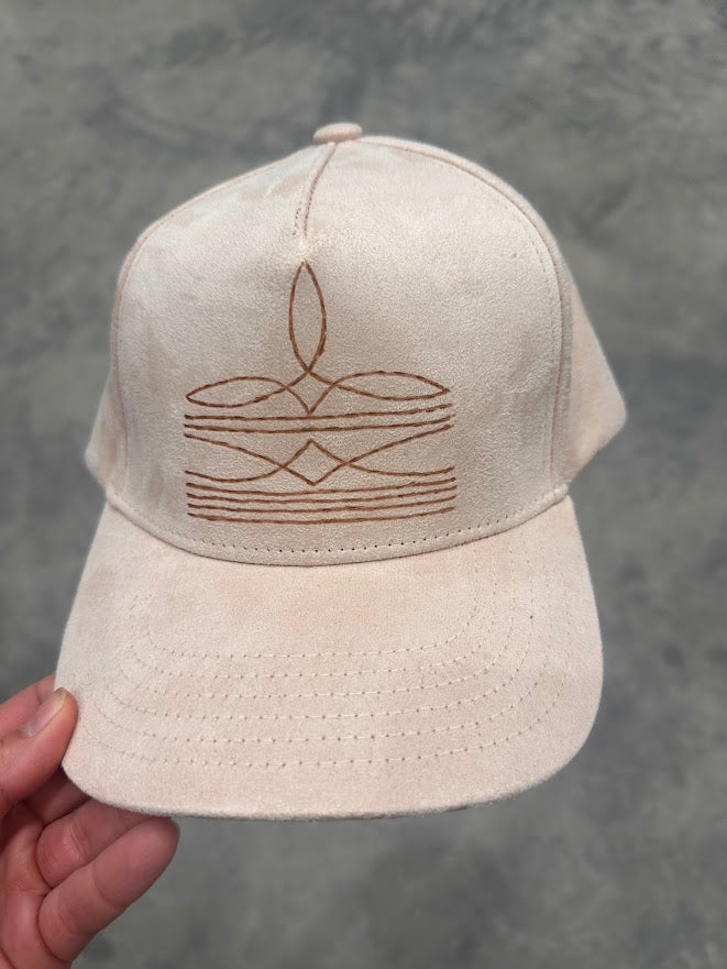 Beige cap with brown embroidered design held against a gray background