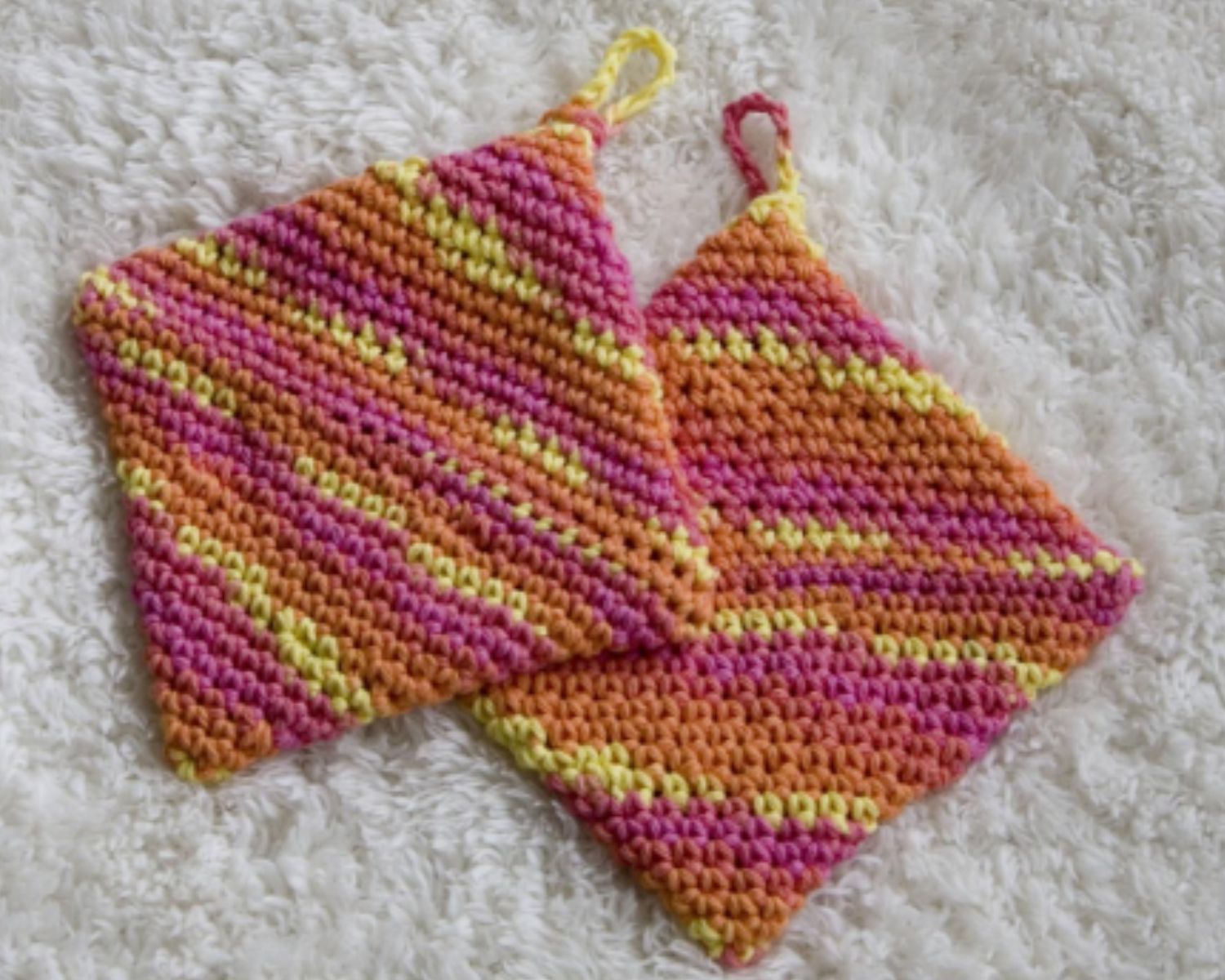 Pair of colorful crocheted pot holders on a textured white surface